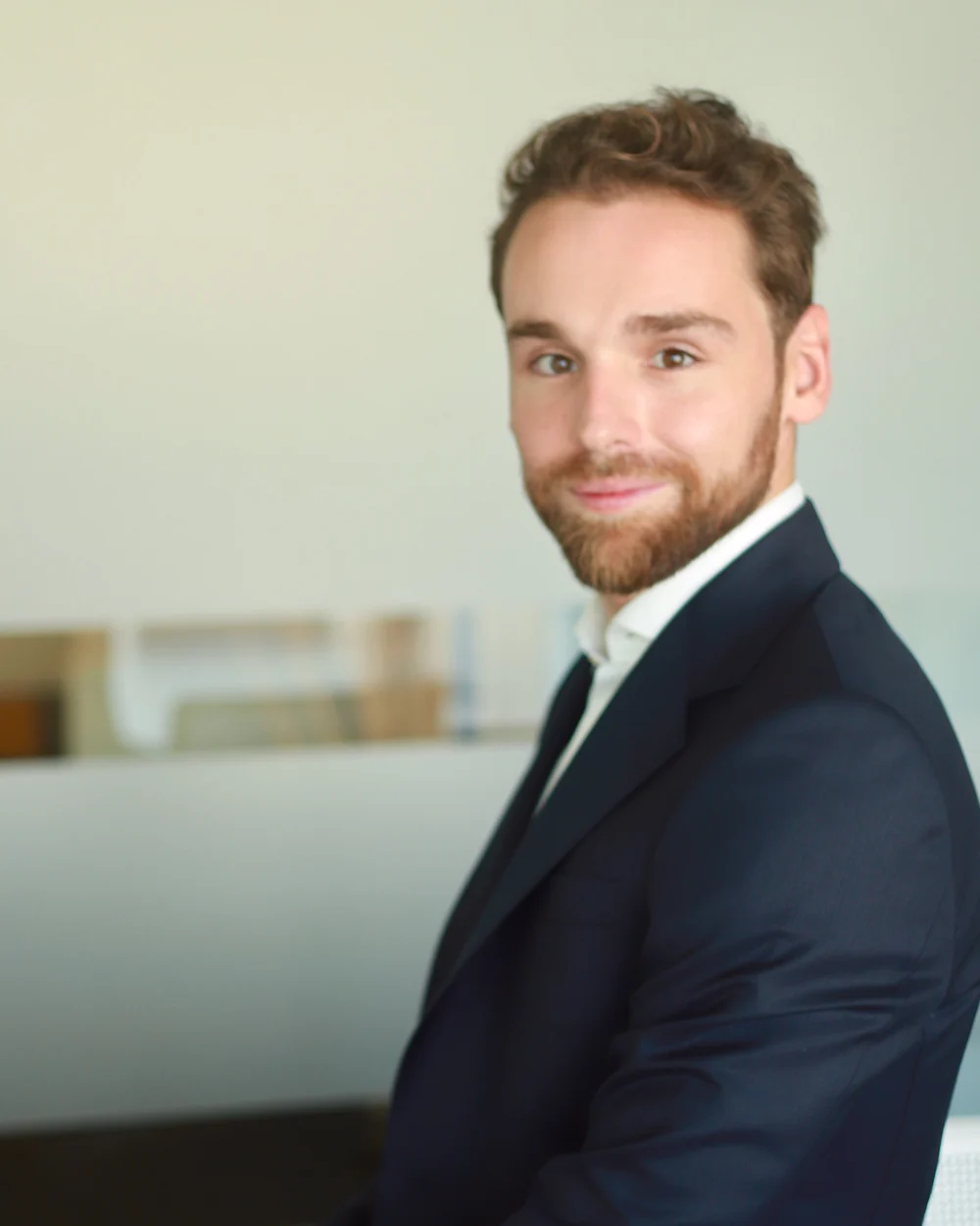 Carlos Pascual Adell, fundador de The Beacon Holding, de traje azul marino y camisa blanca, sonríe a cámara en una oficina luminosa